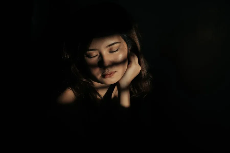 A woman in shadow, hands to her face, in soft light